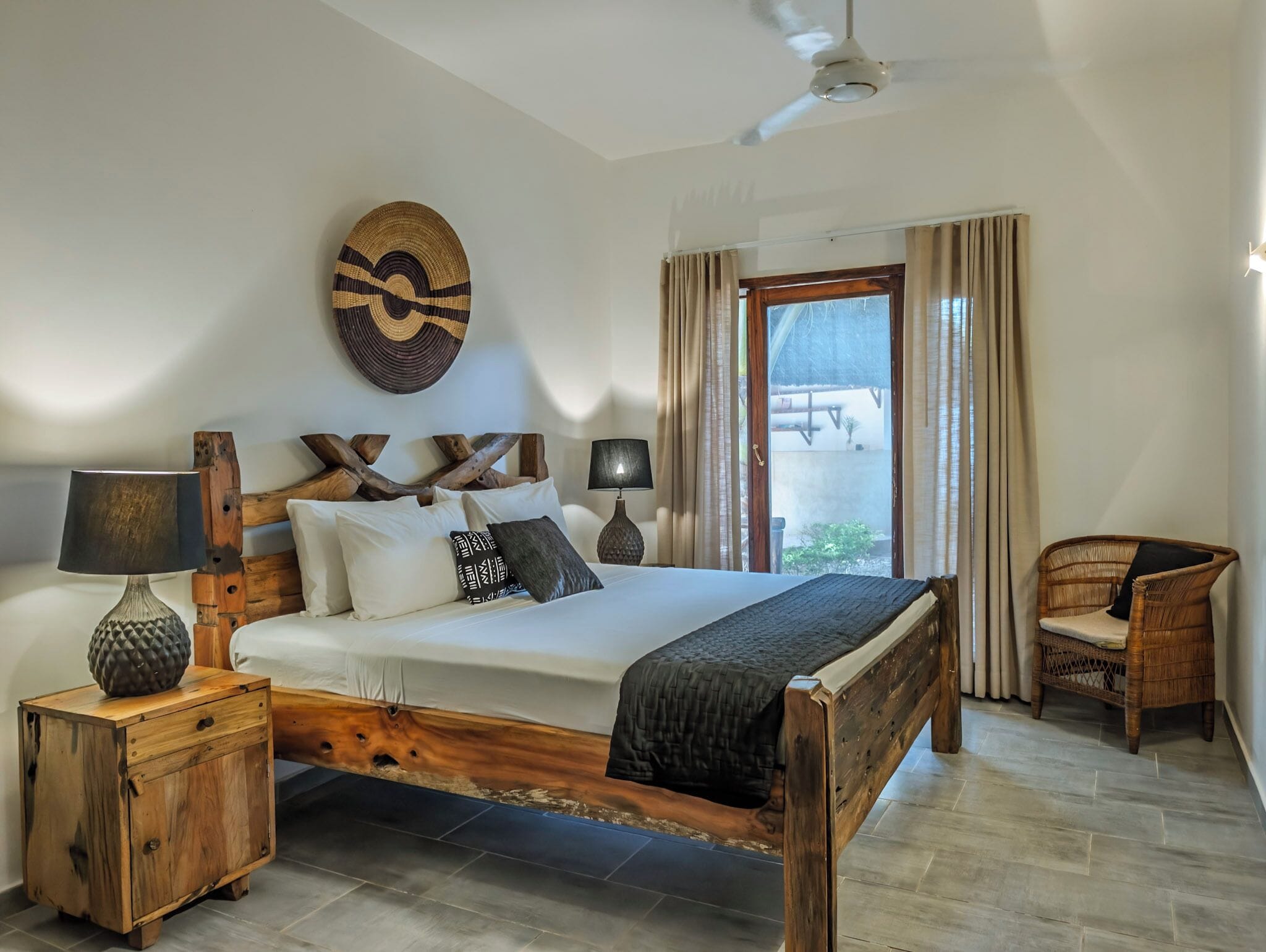 A wooden bed with a headboard, bedside tables, a woven wall hanging, and a wicker chair.