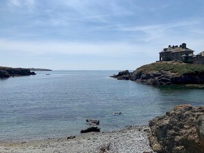 A coastal scene with a large building on a rocky outcrop, calm water, and a clear sky. - Spectacular Sea View Apartment with free Parking - Pass the Keys (Bae Trearddur)