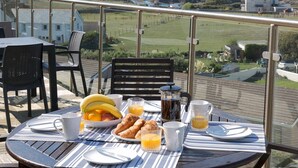 Ett frukostbord med croissanter, frukt och drycker på en balkong med utsikt över ett vackert landskap.