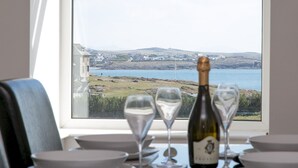 Ett bord med en vinflaska och vinglas, med utsikt över en kustlinje med hus och vatten.
