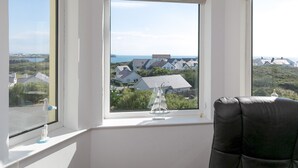 Ett rum med ett stort fönster med utsikt över ett kustnära område, ett litet bord med en dekorativ detalj och en svart stol.