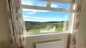 A room with a large window offering a view of a green landscape, a radiator below, and a wicker chair to the left. - Beautiful 5BR Rural Cottage with Outstanding Views - Pass the Keys (Castle Douglas)