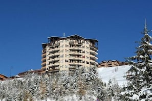 A multi-story hotel with balconies, surrounded by snow-covered trees and a clear blue sky. - 2nd floor, balcony, tv, ski locker, 18m², Les Menuires (Les Menuires)