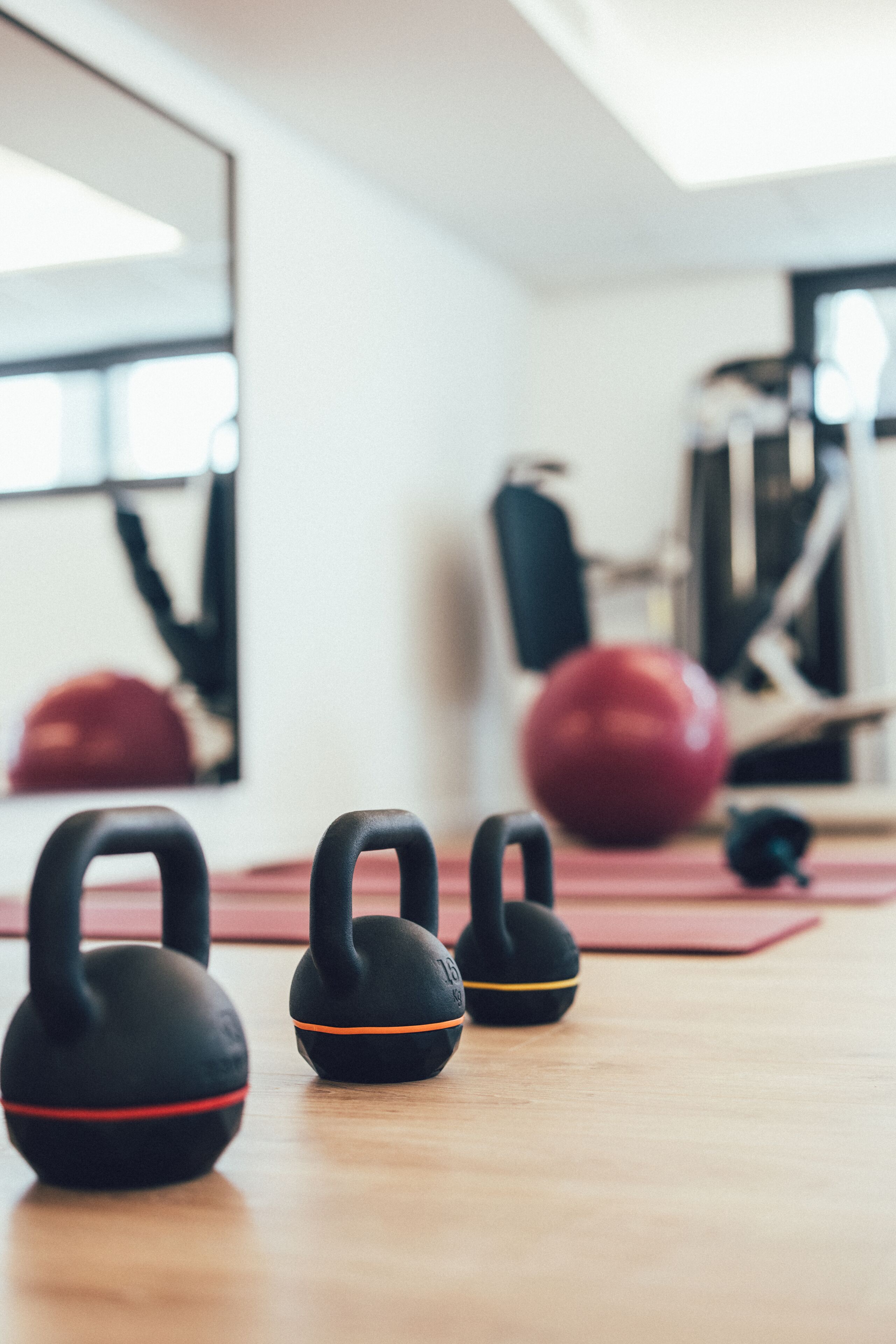 A gym with kettlebells, a red exercise ball, and a mirror on the wall.