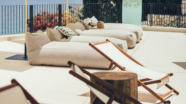 A sunlit outdoor seating area with lounge chairs and a large umbrella, overlooking a scenic view of the sea and greenery. - Cala Lanuza Suites (El Campello)