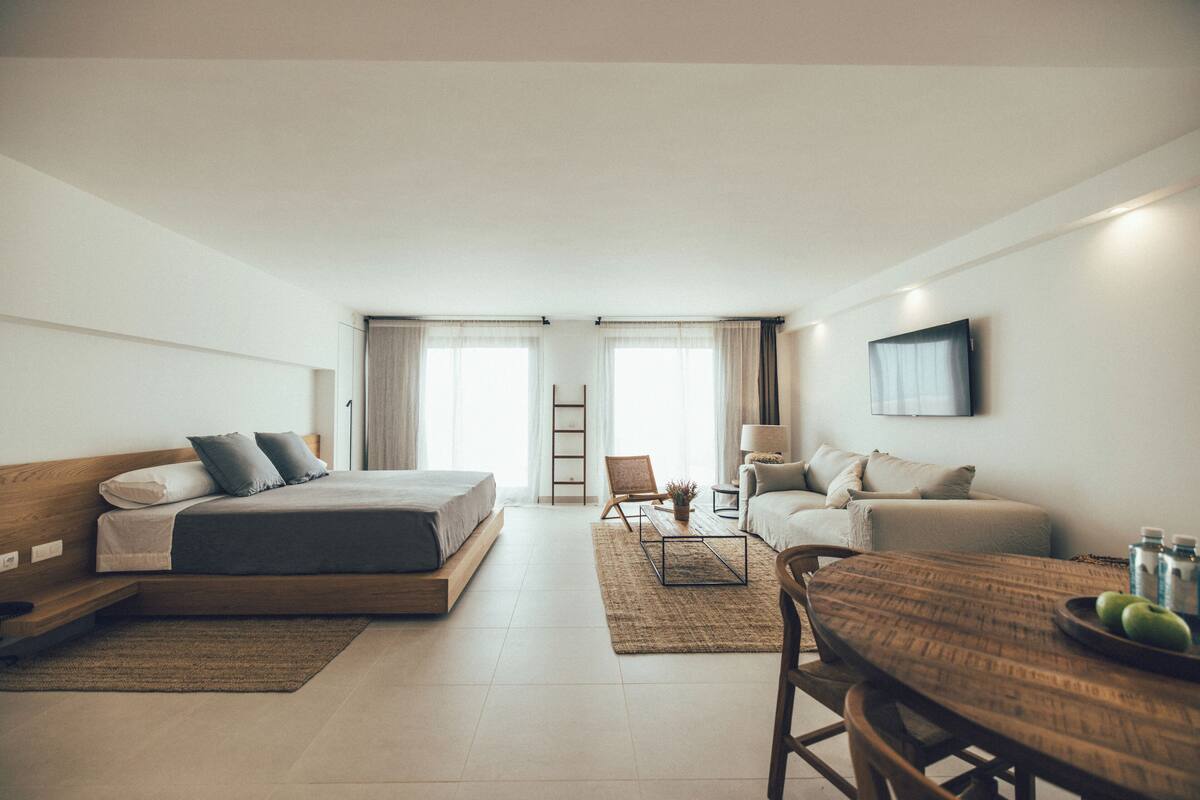 Ein modernes Hotelzimmer mit Bett, Sofa, Esstisch und Fernseher.