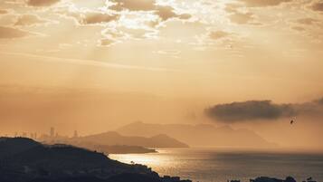 A coastal cityscape at sunset with a view of the ocean and distant mountains.
