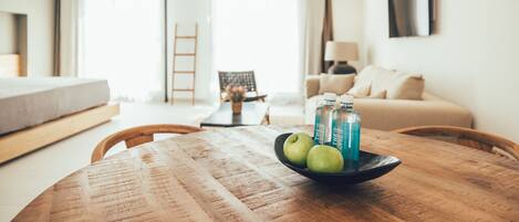 Una sala de estar moderna con una mesa de comedor de madera, un sofá y una cama. Hay una ventana con cortinas, un televisor montado en la pared y una escalera al fondo.