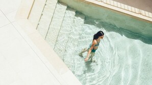 A person in a swimming pool with clear water and tiled steps leading into the pool. - Cala Lanuza Suites (El Campello)