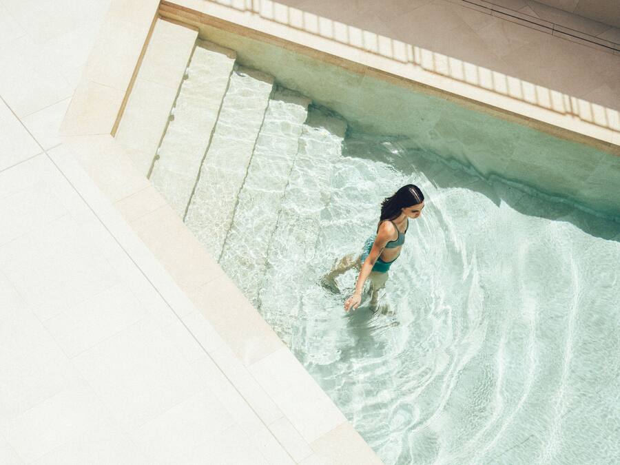 Una persona en una piscina con agua cristalina y escalones de cerámica que bajan al agua.