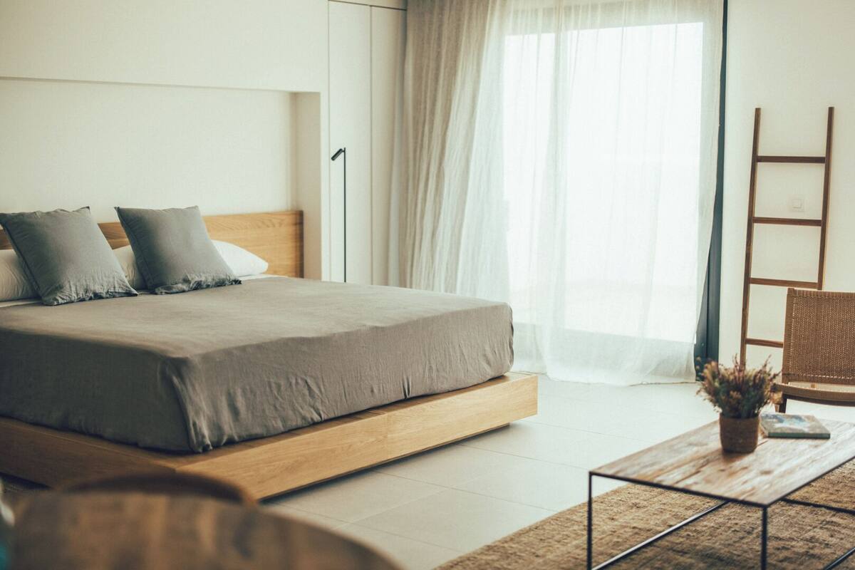Ein modernes Schlafzimmer mit einem großen Bett, einem Holz-Kopfteil, einem Nachttisch mit Pflanze und einer an der Wand stehenden Leiter.