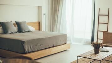 Une chambre à coucher moderne avec un lit, une table de chevet, une chaise et une fenêtre ornée de rideaux légers.