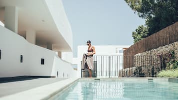 A modern pool area with a clear view of the pool, a person standing by the pool, and a white building in the background.