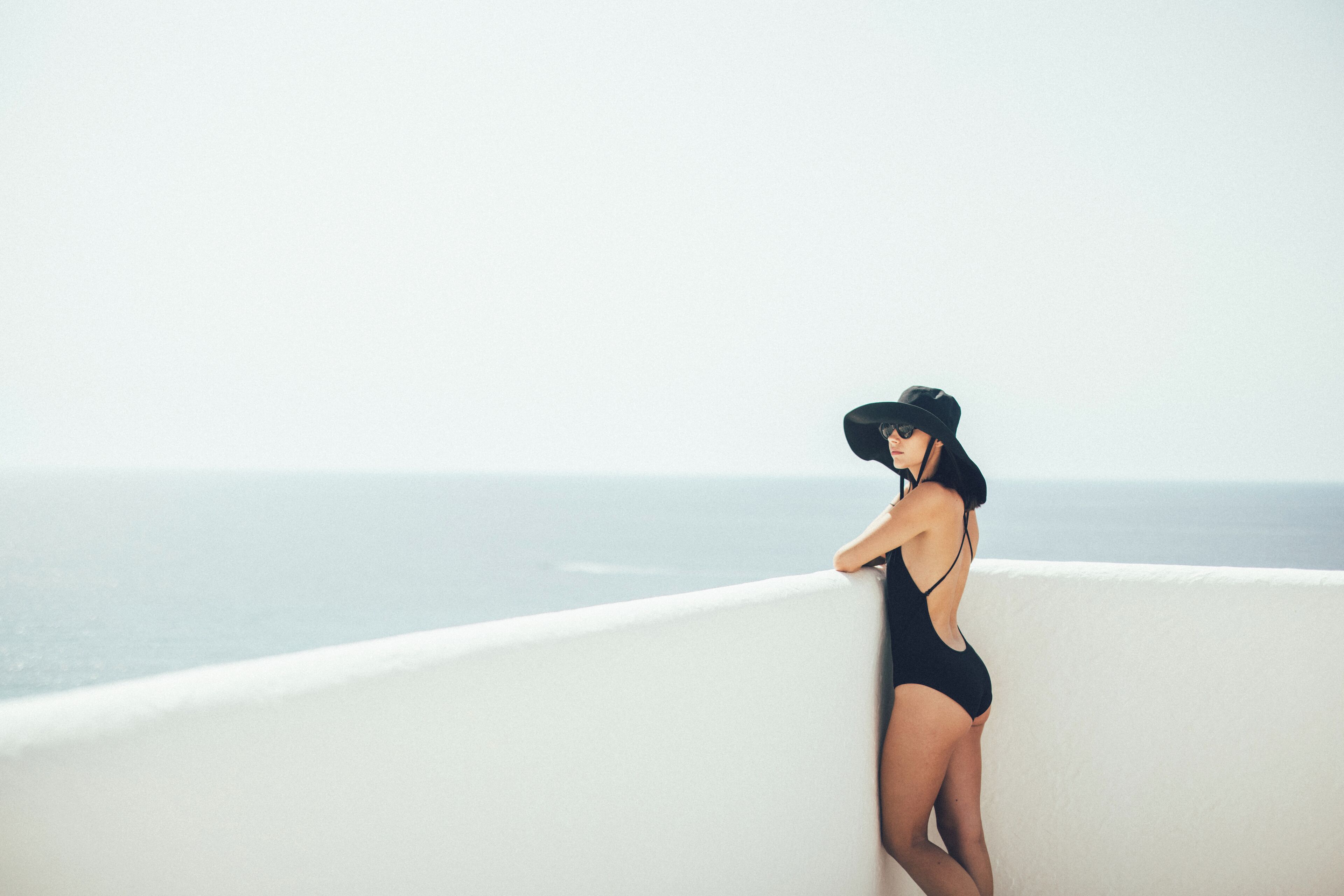 A person in a black swimsuit leaning on a white balcony with a view of the ocean.