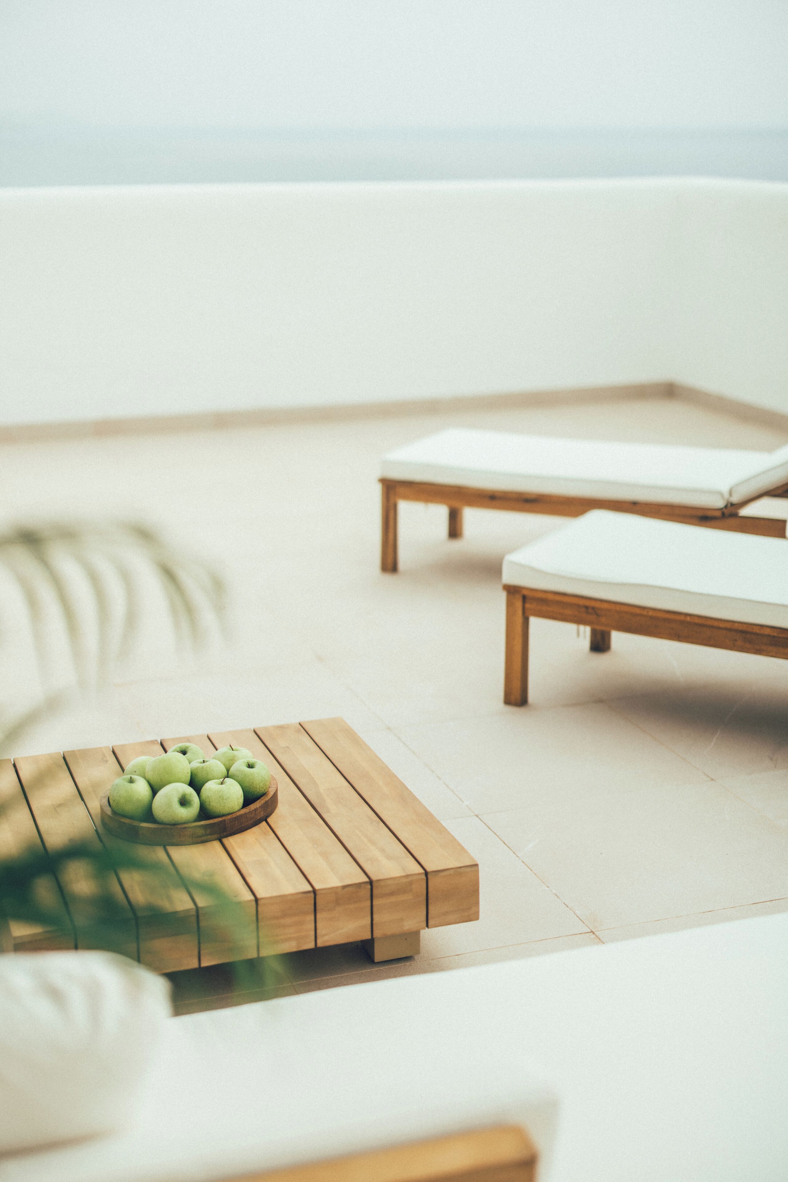 Een houten tafel met een schaal groene appels, twee houten lounge fauteuils en een witte vloer.