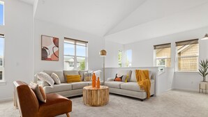 Ein geräumiges Wohnzimmer mit einem Ledersessel, einem runden Holztisch und zwei Sofas mit Kissen.