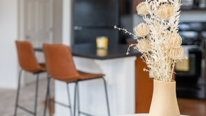 Eine moderne Küche mit einer zentralen Kochinsel, zwei orangefarbenen Stühlen und einem Tisch mit einer Vase mit getrockneten Blumen.