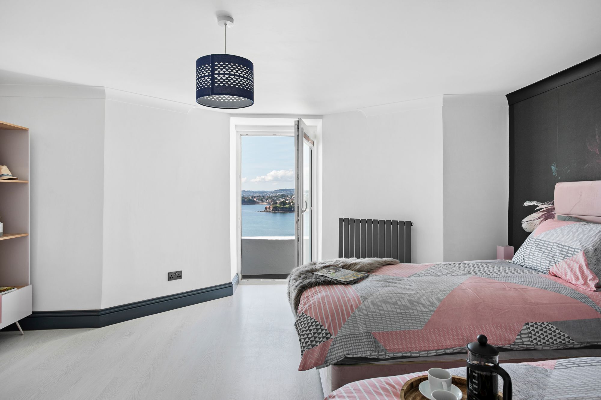 Een moderne slaapkamer met een groot bed, uitzicht op zee, een radiator en een plank met boeken.