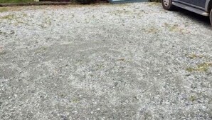 Een gebouw met twee verdiepingen, een grindpad en een geparkeerde auto.