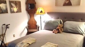 Een slaapkamer met een groot bed, een houten hoofdeinde, een lamp en een schilderij van een eland.