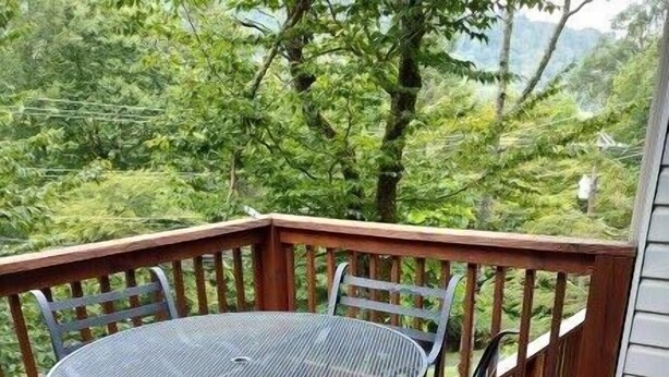 Een ronde metalen tafel met vier stoelen op een houten terras, met een houten leuning.