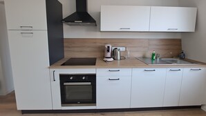 A modern kitchen with white cabinets, a black oven, a stainless steel range hood, a countertop with a coffee maker, and a sink.