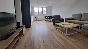 A modern living room with a flat-screen TV, a sofa, a coffee table, and a dining area with chairs and a table.