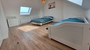 A bedroom with two beds, wooden flooring, a skylight, and pendant lights.