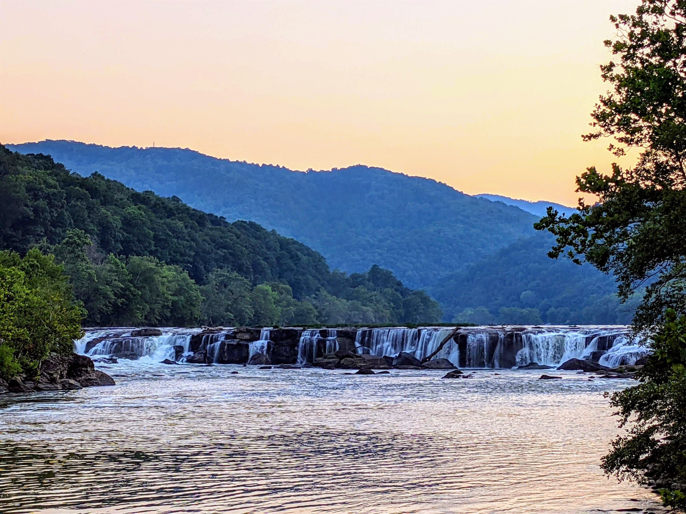 A waterfall with multiple cascades surrounded by lush greenery and hills in the background.