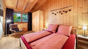 Een houten kamer met een bed, een stoel, een bureau en een raam.