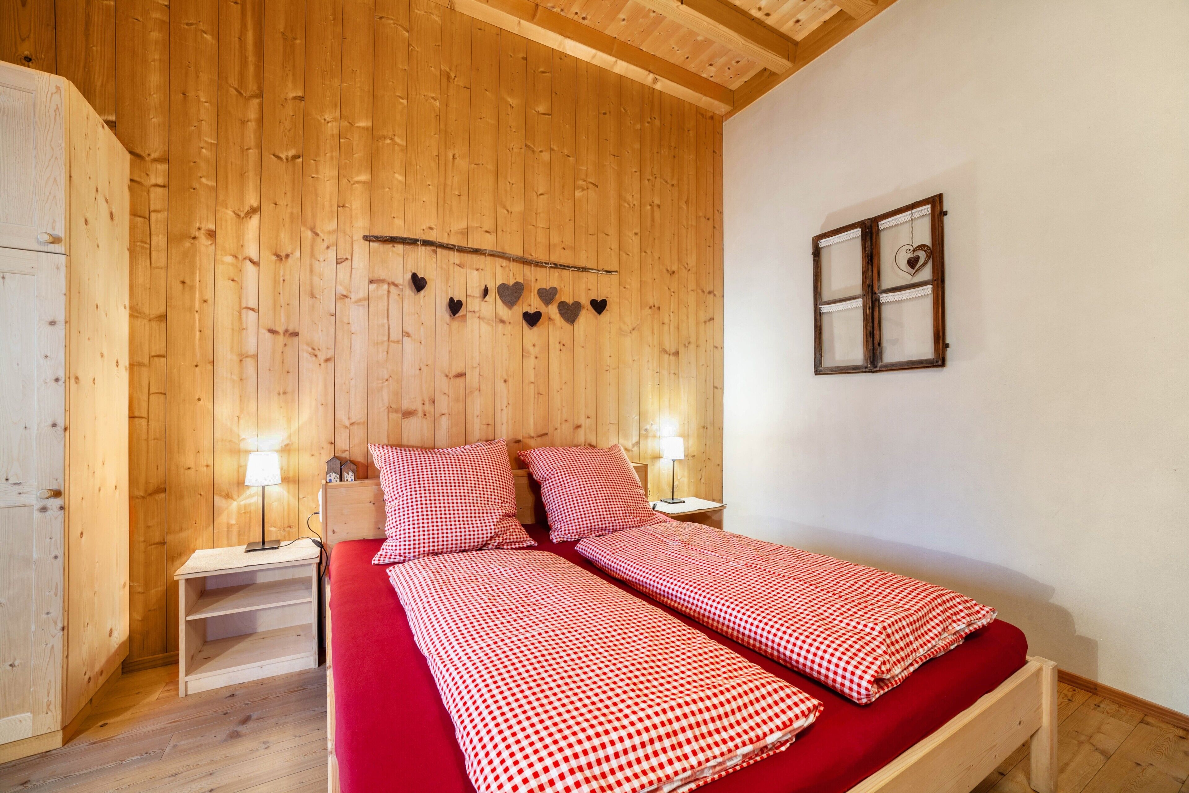Een kamer met houten lambrisering, een bed, twee nachtkastjes, een wandplank en een raam met een hartdecoratie.
