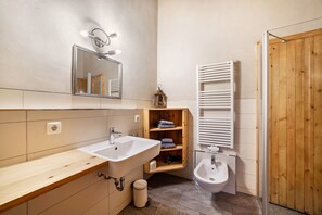 Une salle de bain avec un meuble-lavabo en bois, un évier, un bidet, un miroir et un placard en bois contenant des serviettes.
