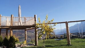 Een houten terras met een schommel, een picknicktafel en uitzicht op bergen.