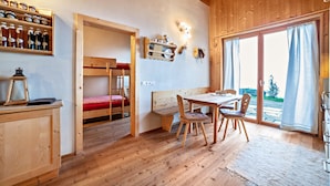 Een houten interieur met een stapelbed, een eettafel met stoelen, en een plank met flessen.