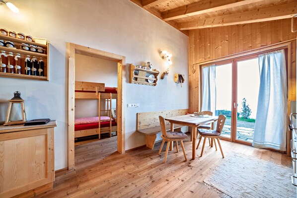 Un intérieur en bois avec un lit superposé, une table à manger avec des chaises et une étagère avec des bouteilles.