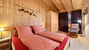 Una habitación de madera con una cama, una silla y una mesita de noche con lámpara.