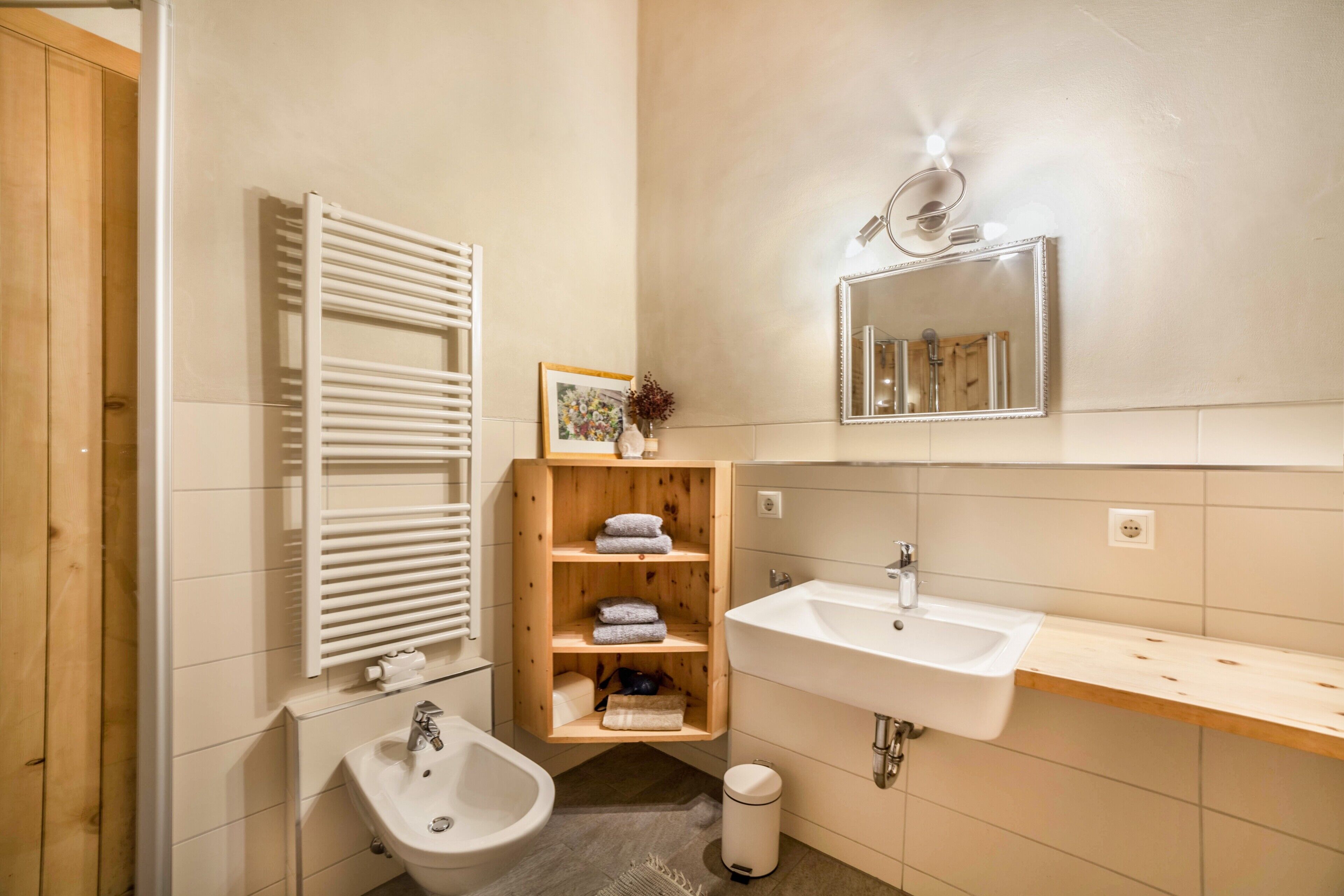 Baño con bidé, lavamanos, espejo y estante de madera con toallas.