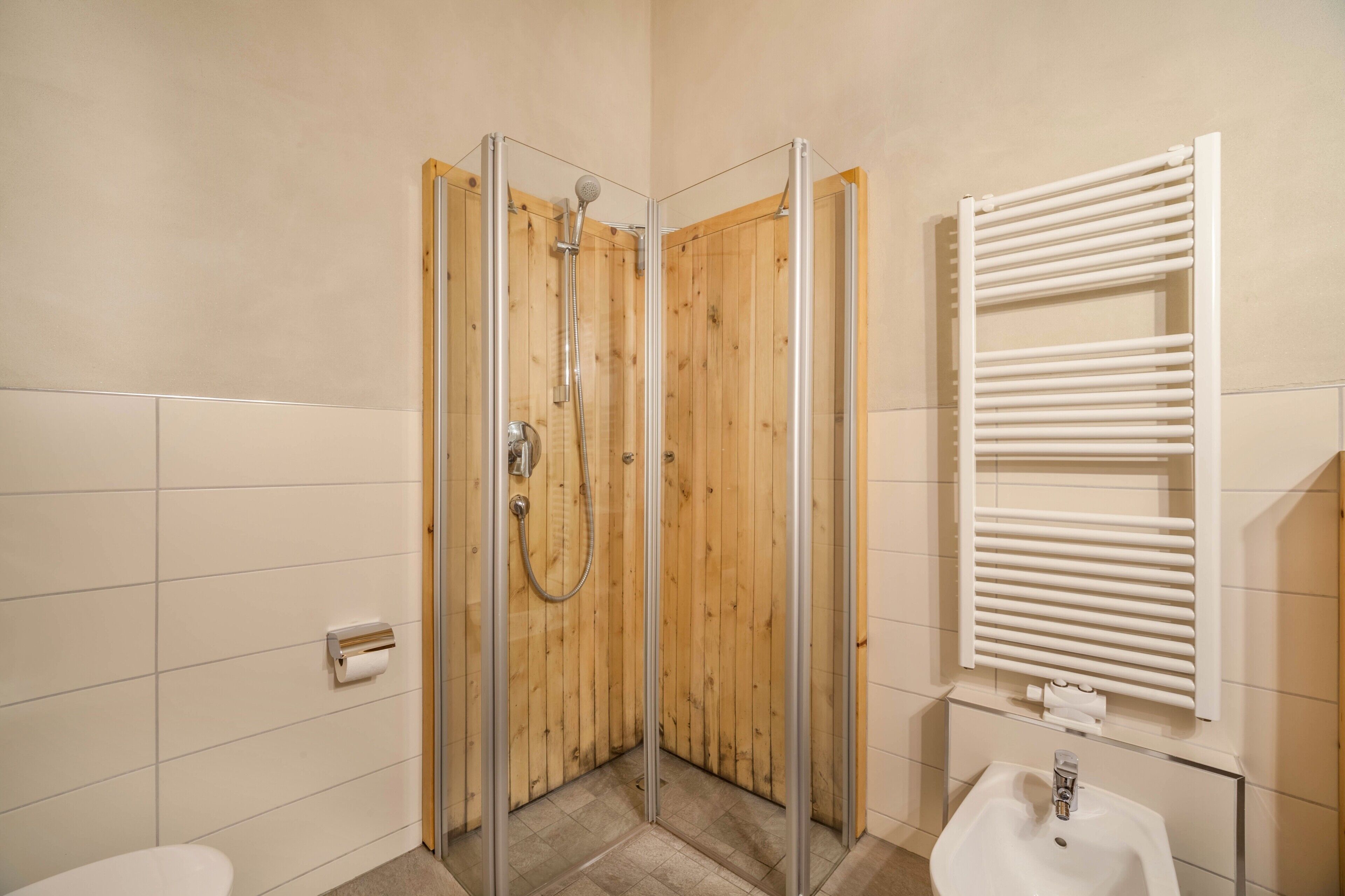 Eine Dusche mit Glastüren, ein weißes Waschbecken und ein Handtuchhalter.