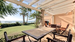 Um pátio externo com mesa e cadeiras, vista para o oceano e uma estrutura de pérgula.