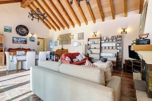 Ein Wohnzimmer mit Sofa, einem roten Sessel, einem Essbereich mit Tisch und Stühlen, einem Bücherregal und einem Fernseher.