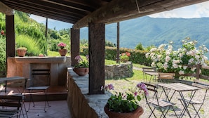 An outdoor patio with a stone table and chairs, surrounded by potted plants and a view of mountains. - Agriturismo "Universal Harmony - Pettirosso" with Mountain View and Shared Pool (Dicomano)
