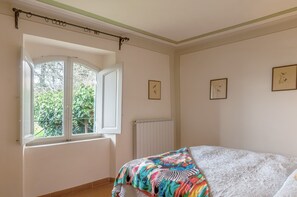 Un dormitorio con cama, ventana, radiador y cuadros en la pared.