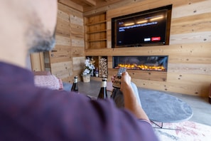 Eine Person sitzt auf einem Sofa in einem Holzraum mit Fernseher und Kamin.