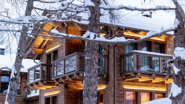 A multi-story wooden building with balconies, surrounded by snow-covered trees.