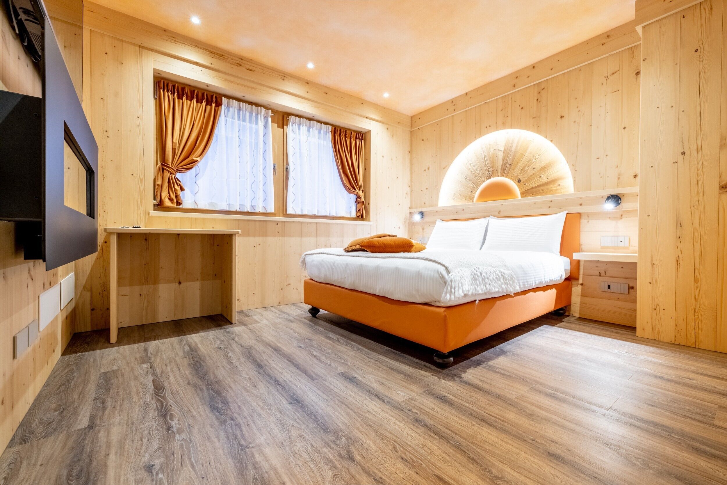 A wooden-paneled room with a bed, a desk, and a large window with curtains.