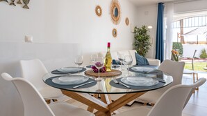 A dining area with a glass table, white chairs, and a bottle of wine.