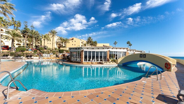 A swimming pool with a tiled deck, palm trees, and a building with large windows.