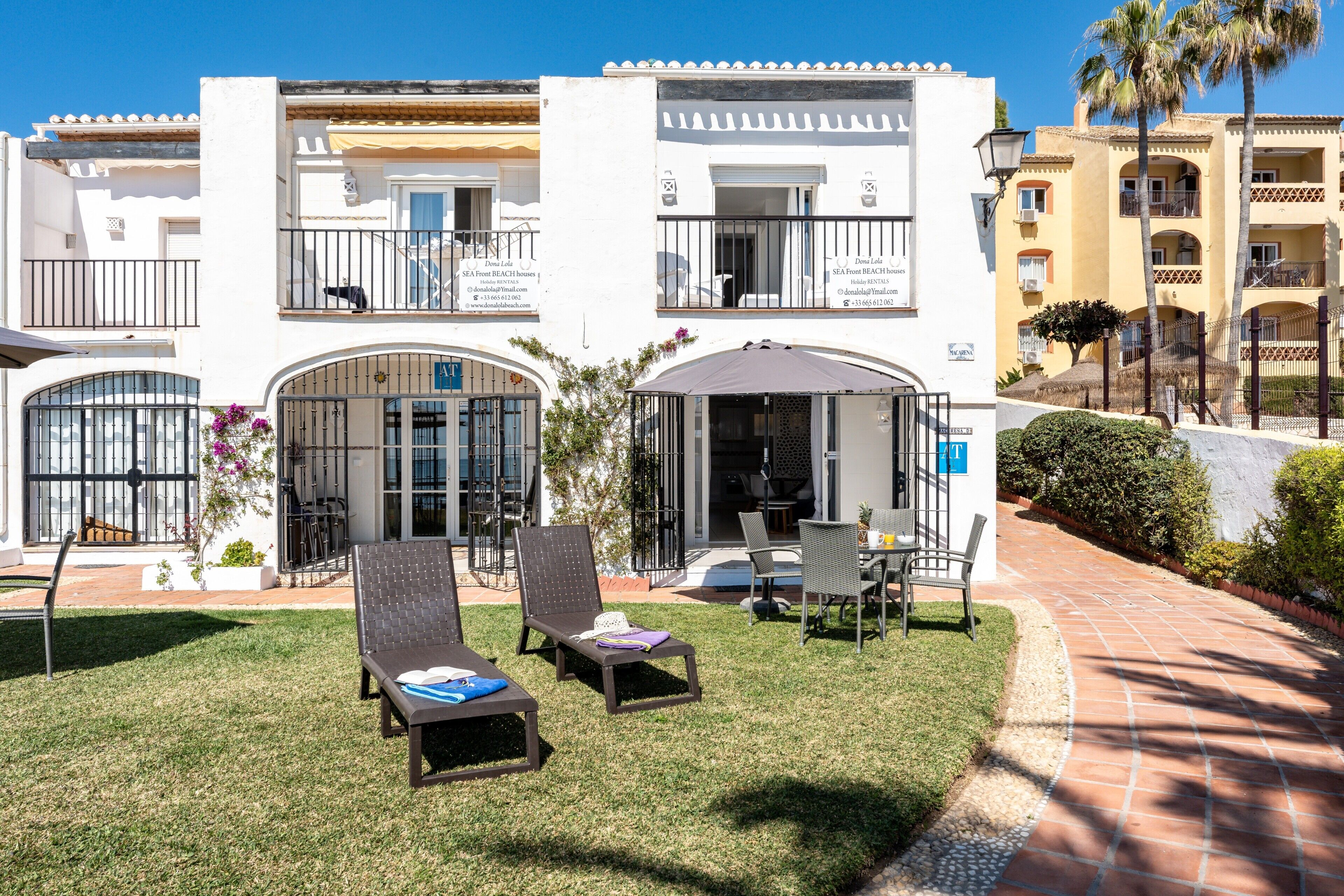 A hotel with a covered outdoor seating area, a pool, and a well-maintained lawn.