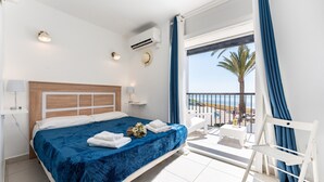 A bedroom with a bed, a bedside table, a nightstand, a window with curtains, and a balcony with a chair.