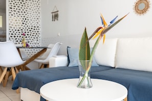 En moderne stue med en hvid sofa, et rundt hvidt bord og en glasvase med en paradisfuglblomst.